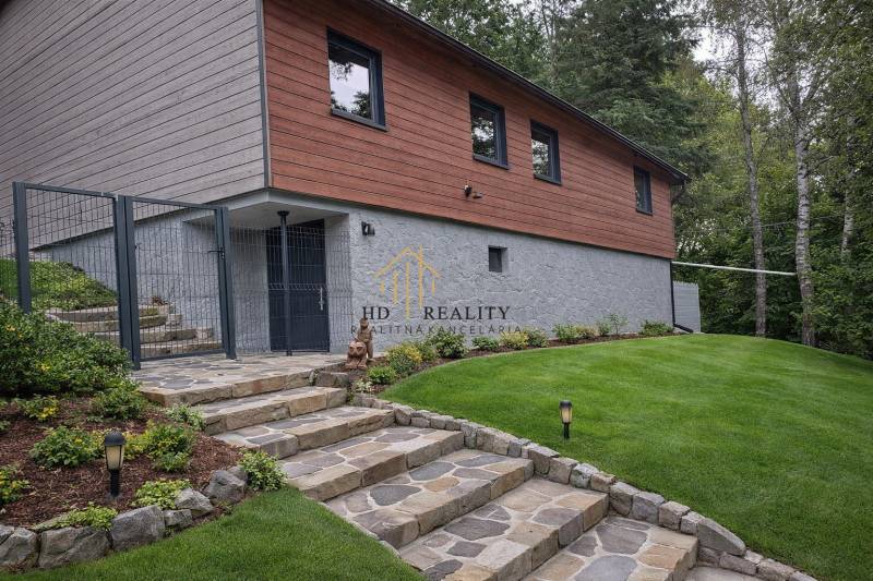 The exterior of the cottage near Zvolen with stone steps, wooden cladding, and a well-maintained lawn.