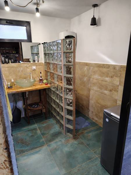 A bathroom in a cottage with a sink, a glass partition, and colorful tiles.