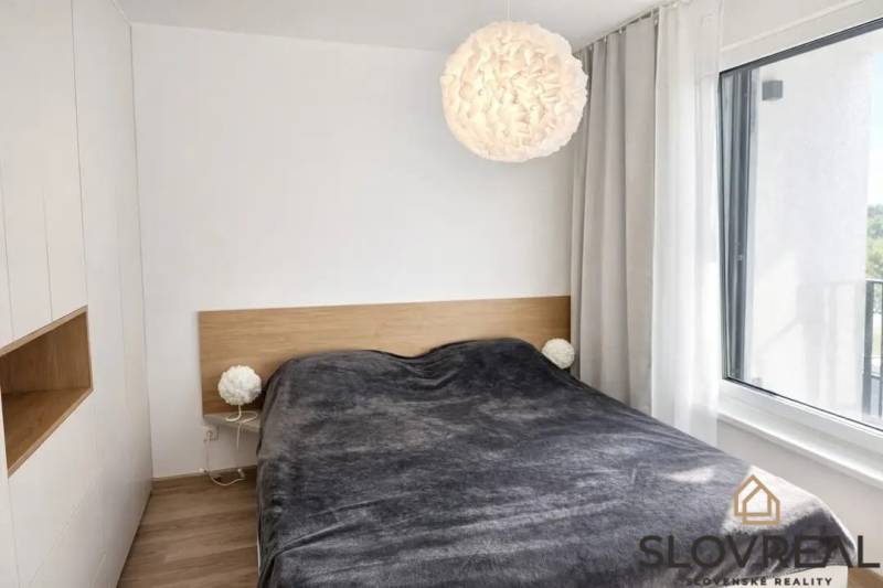 A bedroom in a one-room apartment with a bed, a lamp, and a wooden decor floor.