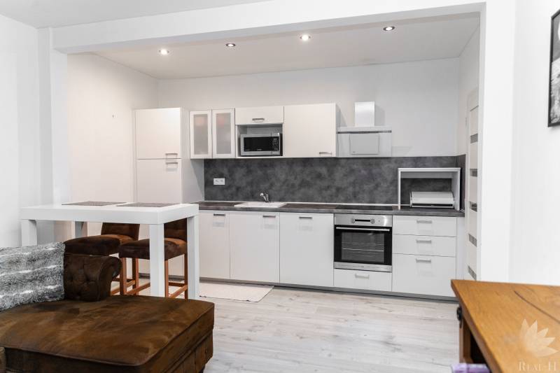 A modern kitchen in a studio apartment with white furniture and a wooden decor floor.