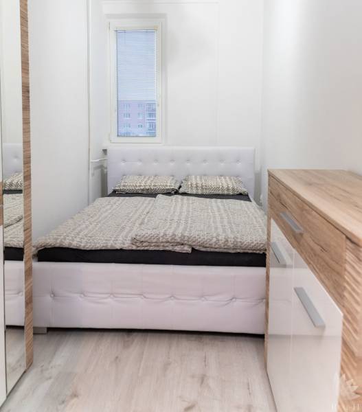 Bright bedroom with a bed, wooden decor, and a dresser in a studio apartment.