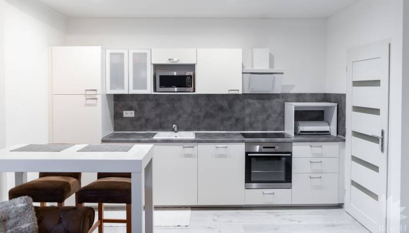 A kitchen with white cabinets, a bar table, and a wood-patterned floor in a studio apartment.