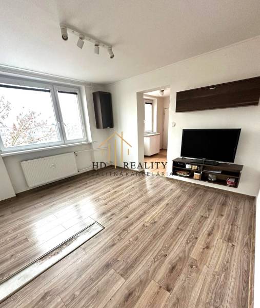 Living room in a 4-room apartment with a TV, furniture, and a floor with a wood decor.
