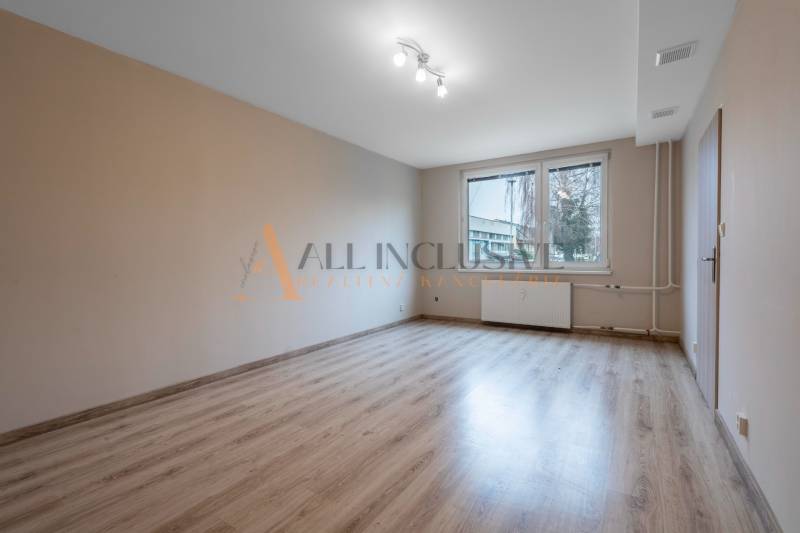 A bright room with wood-patterned flooring and a large window in a studio apartment.