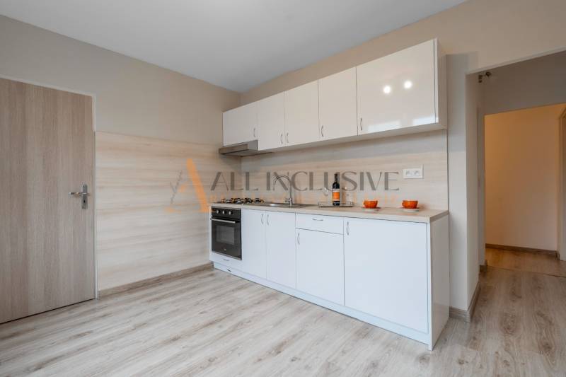 A kitchen with white cabinets in a studio apartment, floor with wood decor.