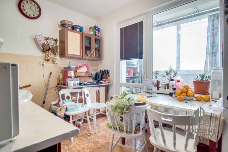 A kitchen in a 2-room apartment with a dining table, flowers, and a floor with a wooden decor.