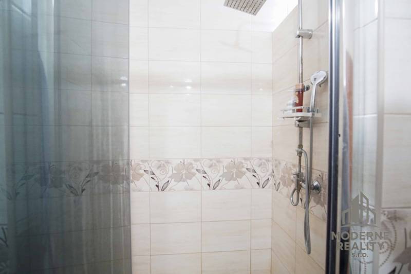 Shower enclosure in a 2-room apartment with decorative ceramic tiles and a rain showerhead.