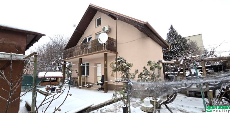 A family house covered in snow in Trnava with a wooden balcony and a garden.