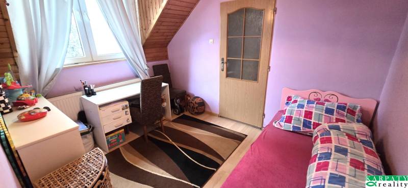 Children's room in the attic of a family house with a table, bed, and carpet.