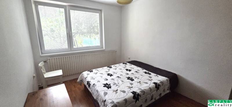 Bedroom with a bed and floral blanket, wooden decor floor, large window.