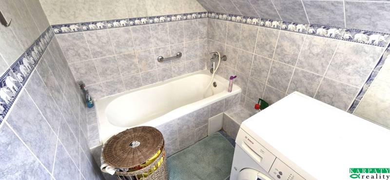 A bathroom with a bathtub, washing machine, and blue-white tiles in a family house.