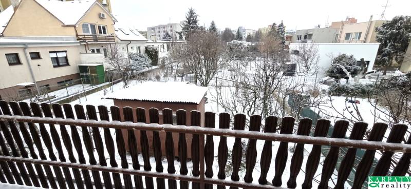 Snow-covered gardens and family houses in Trnava viewed through a wooden fence.