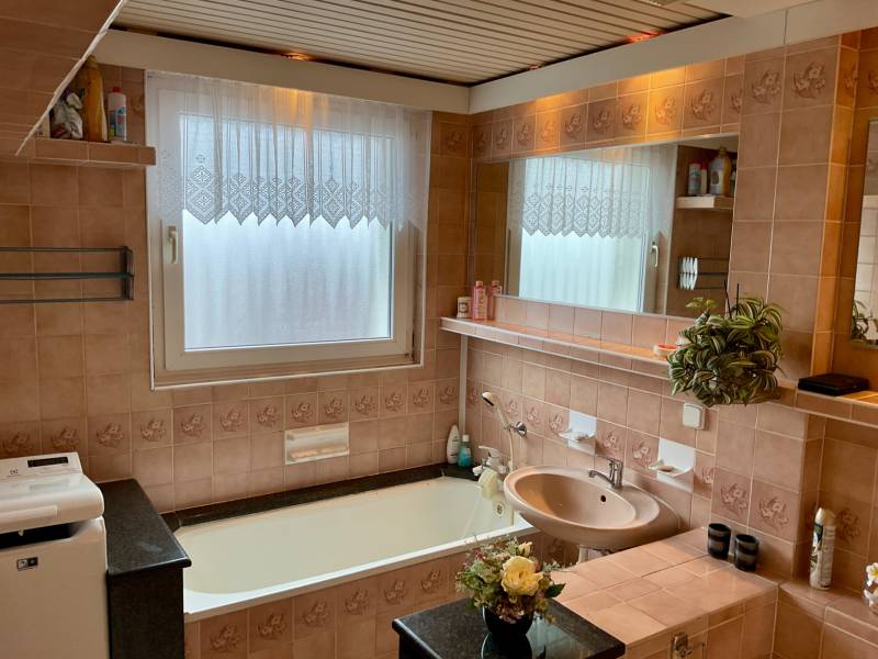 A bathroom in a 3-room apartment with a bathtub, subtly decorated tiles, and a mirror.