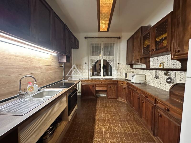 A kitchen in a 3-room apartment with a wood-patterned floor and dark furniture.