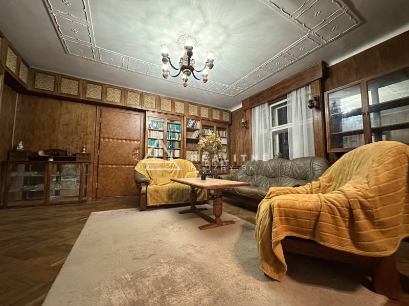 A living room with a wood-patterned floor, wooden paneling, and lots of books.