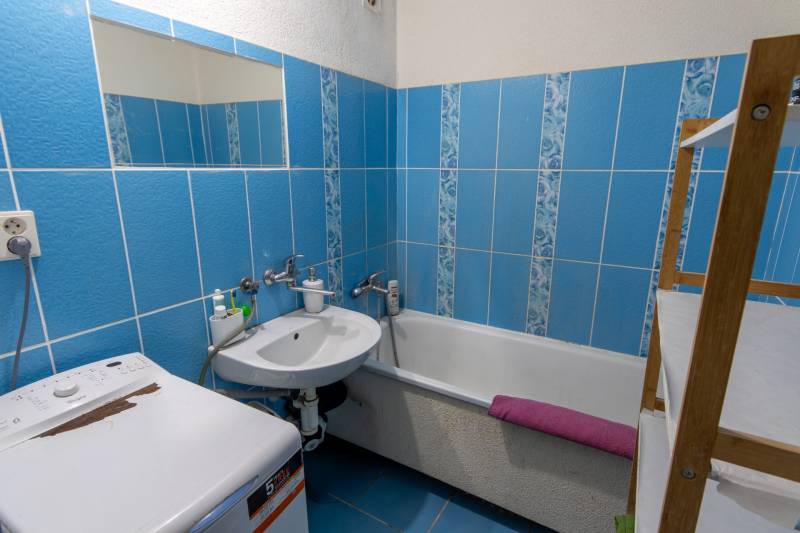 A bathroom in a 2-room apartment with blue tiles, a bathtub, and a washing machine.