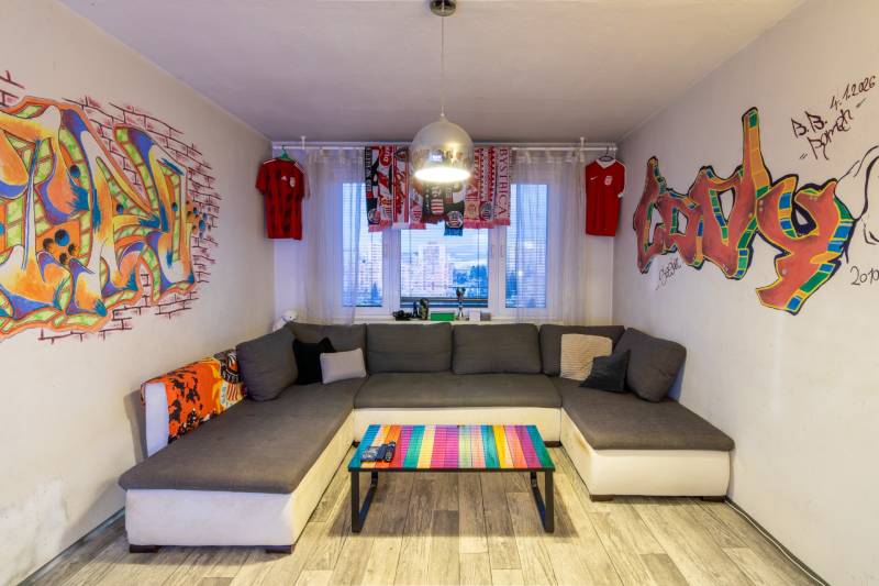 A comfortable living room with graffiti, a gray couch, and a wooden decor floor in a 2-room apartment.