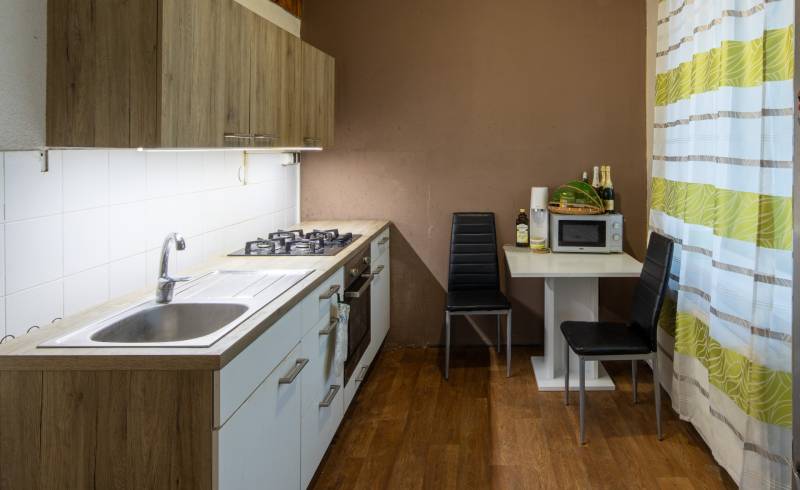 The kitchen of a two-room apartment with a wooden-patterned floor and a dining area.