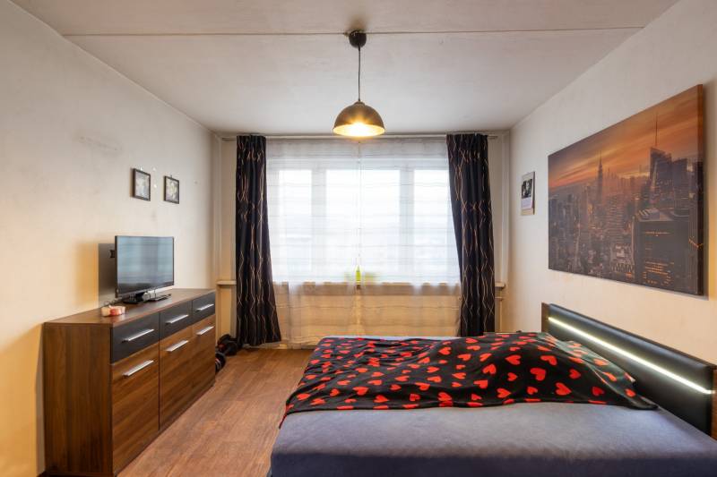 Bedroom with a bed, dresser, and television, wooden decor flooring in a 2-room apartment.