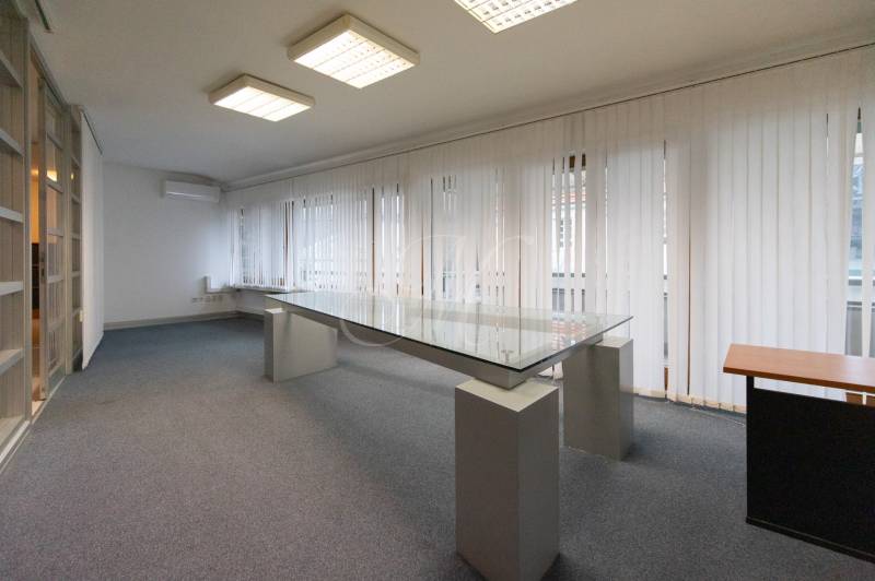 Office room with a glass desk, carpeted floor, and vertical blinds.