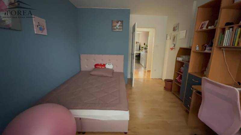 A room in a 3-room apartment with a bed, a shelf, and a floor with a wooden decor.