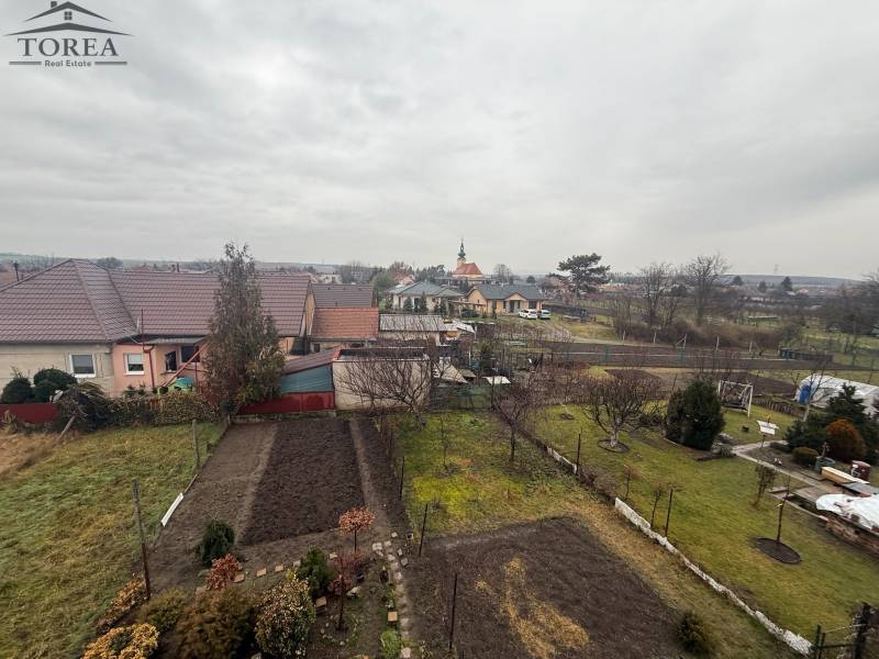 The view from Ludanice to gardens, houses, and a distant tower.
