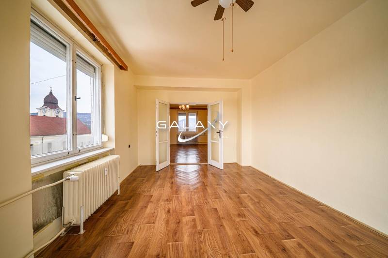 Spacious room in a 2-room apartment with wood-patterned flooring and large windows.