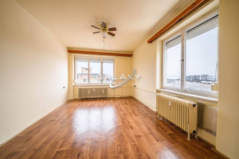 A spacious room with a wooden decor floor and large windows in a 2-room apartment.