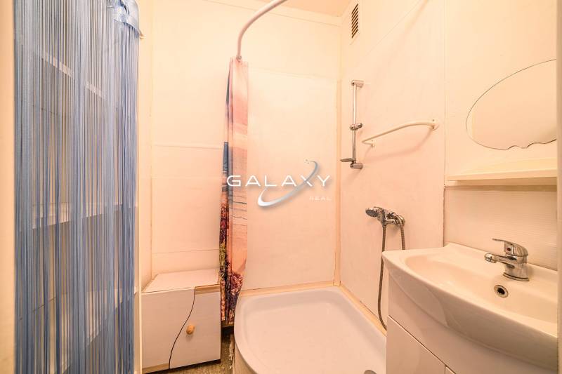 A bathroom in a 2-room apartment with a bathtub, sink, and shower with a plastic curtain.