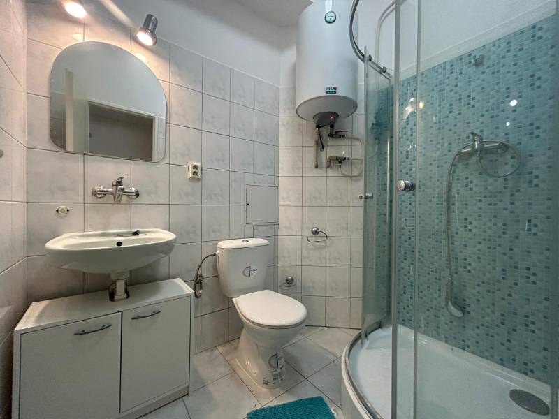 A bathroom with tiles, a sink, a toilet, and a shower in a studio apartment.