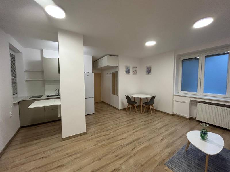 Studio apartment with a kitchenette, table, floor lamp with wooden decor, large window.