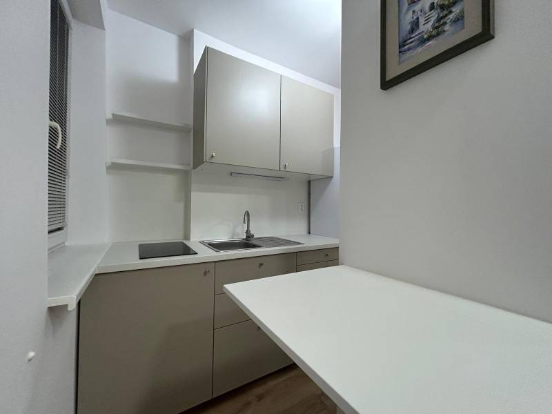 Compact kitchen with grey cabinets, sink, and ceramic hob in a studio apartment.