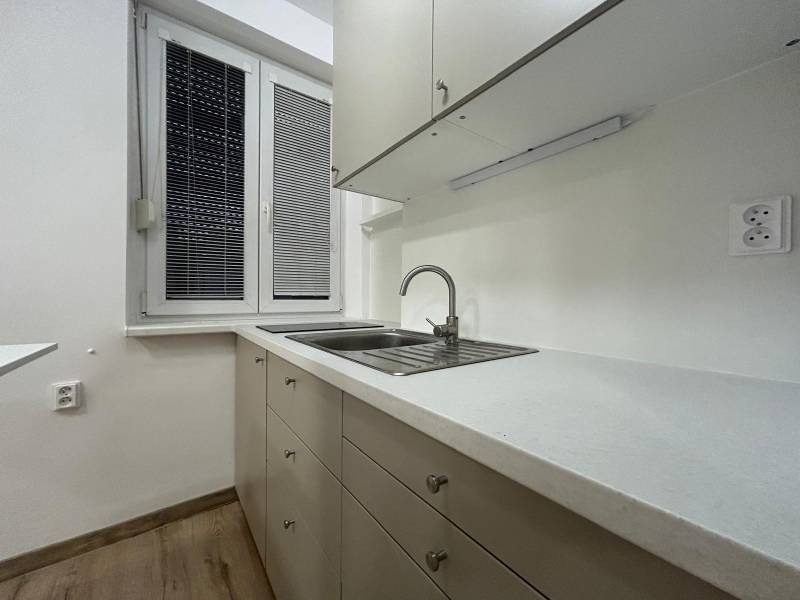 A kitchenette in a studio apartment with white cabinets and a wood-patterned floor.