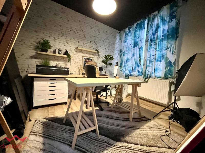 A study in a family house with a large table, plants, and a patterned curtain.
