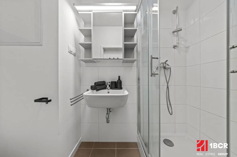 Bathroom with white tiles, a shower enclosure, and a sink.