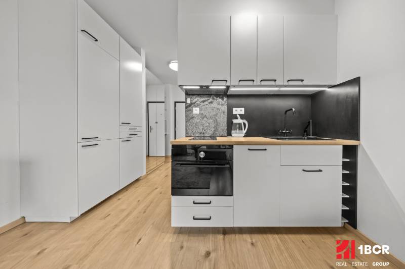 A kitchen in a studio apartment with white cabinets and a wood-patterned floor.