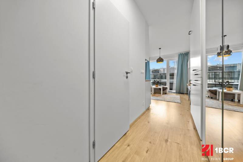 Interior of a 1-room apartment with a wooden decor floor and light furnishings.
