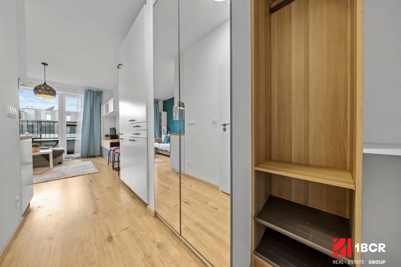 Interior of a 1-room apartment with a wooden decor floor, mirrored wardrobe, and modern furniture.