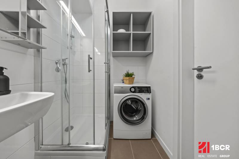 Bathroom with a washing machine, shower cabin, and white walls in a studio apartment.
