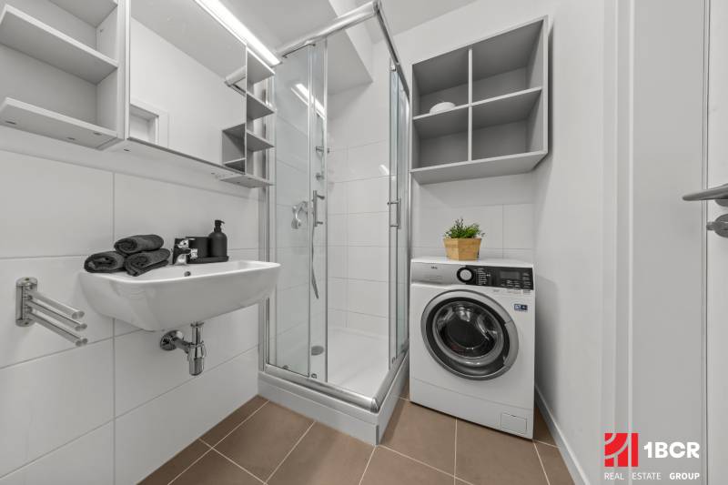 Bathroom with a washing machine, shower, and sink in a studio apartment.