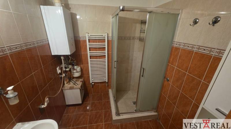 A bathroom with ceramic tiles, a shower corner, and a white boiler in a three-room apartment.
