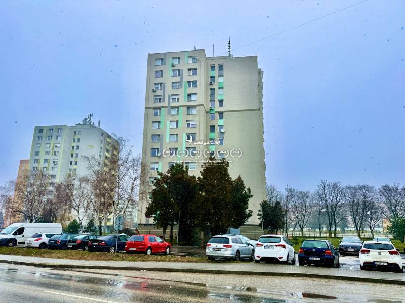 In Nové Zámky on S.H. Vajanský Street, there are tall buildings and parked cars.