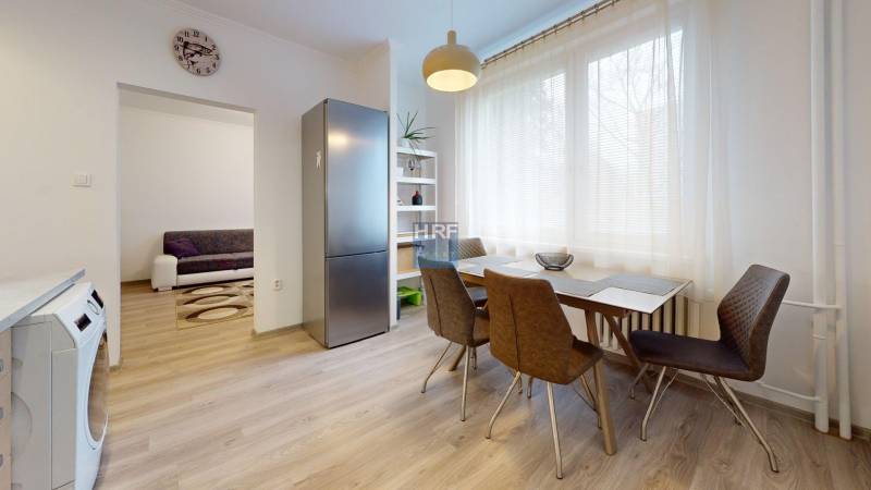 Kitchen of a 2-room apartment with a wooden decor floor, dining table, and refrigerator.