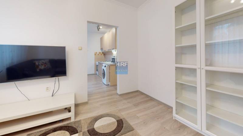 Living room with a TV, wardrobe, and a view into the kitchen in a 2-room apartment.