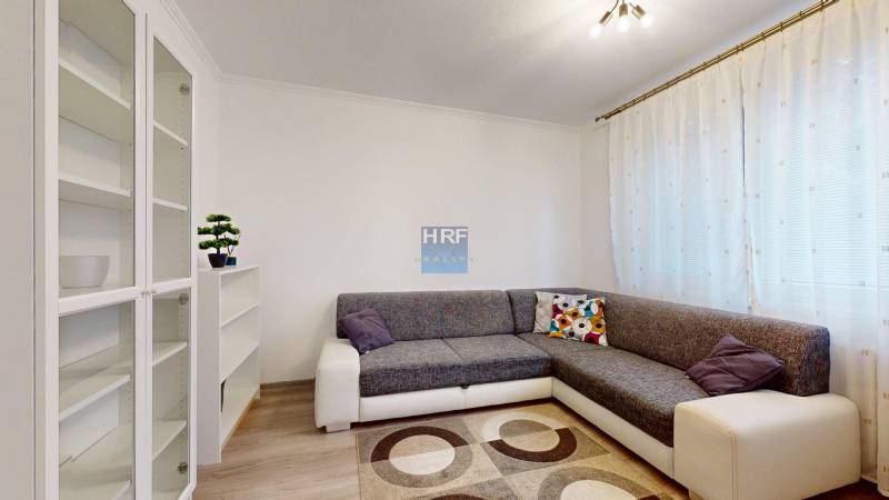 Living room in a two-room apartment with a sofa, shelves, and a floor with a wooden decor.