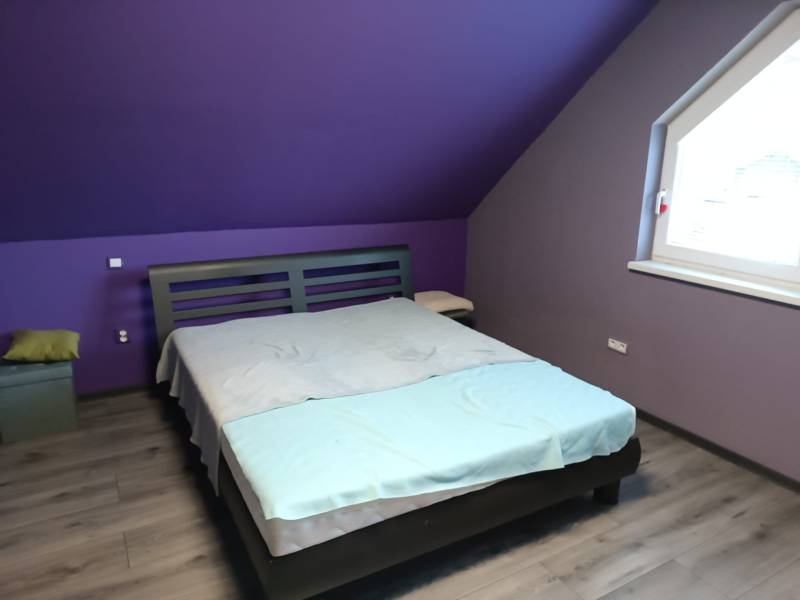 Purple bedroom with a bed and wood-patterned floor in a family house.