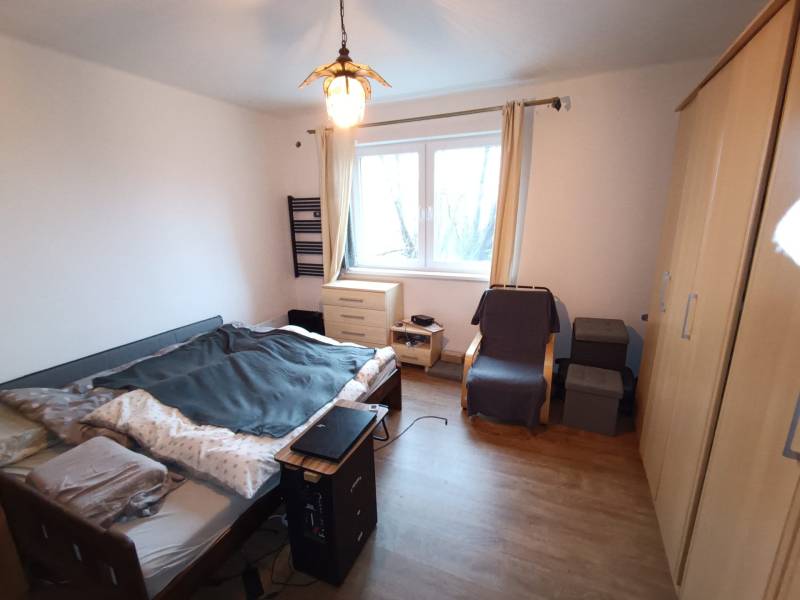 Bedroom in a family house with a bed, wardrobes, an armchair, and a floor with a wooden decor.