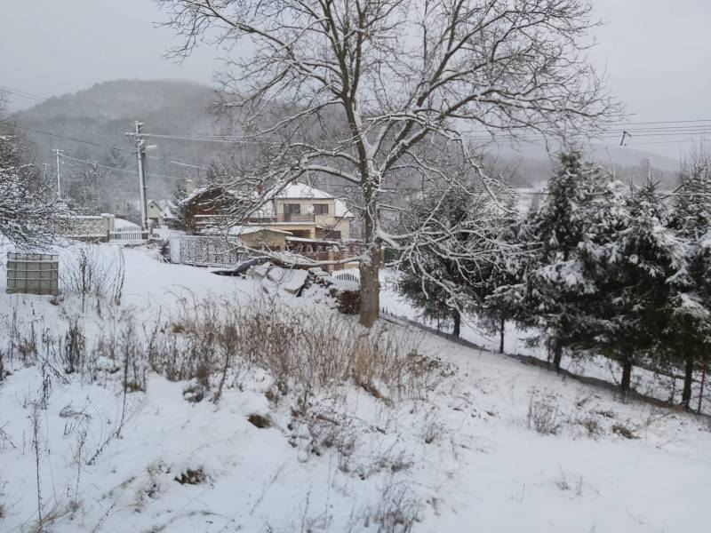 A snowy landscape in Orovnica, with a family house and trees in the background.