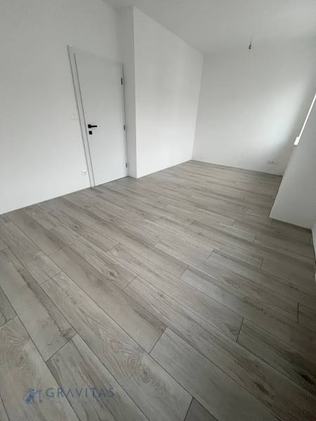 A room in a 2-bedroom apartment with a wood-patterned floor and white walls.