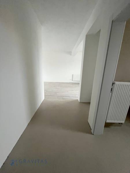 A hallway with white walls and a wooden decor floor in a 2-room apartment.